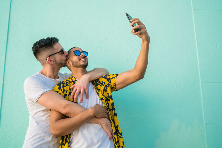 Gay couple taking selfie while standing against wall
