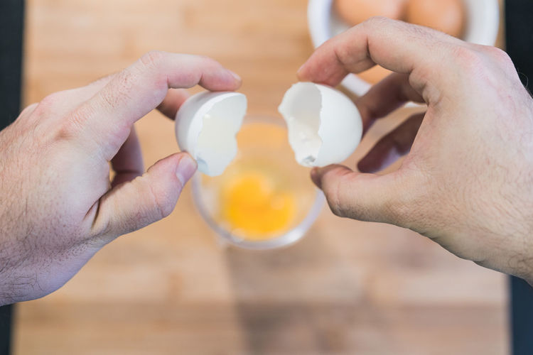 Man cooking in the kitchen in a denim shirt. an anonymous has the eggshell in his hand