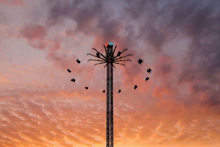 Low angle view of silhouette chain swing ride against cloudy sky during sunset