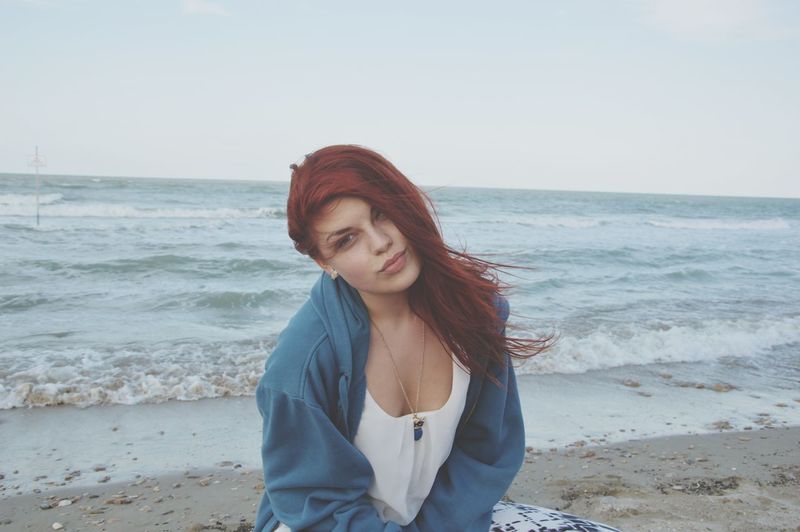 Young woman sitting on sea shore at beach against clear sky