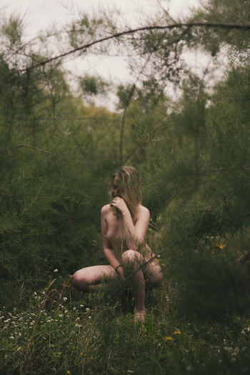 Young naked woman crouching in forest