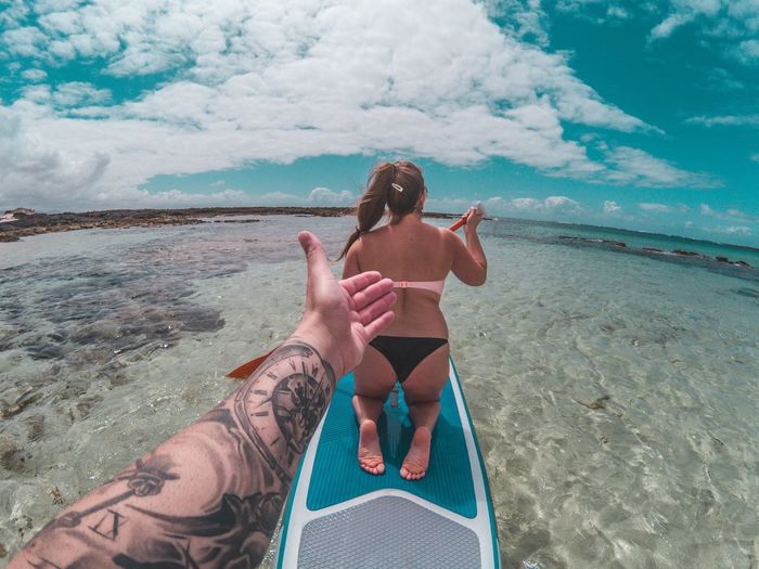 Cropped hand gesturing towards woman paddleboarding on sea