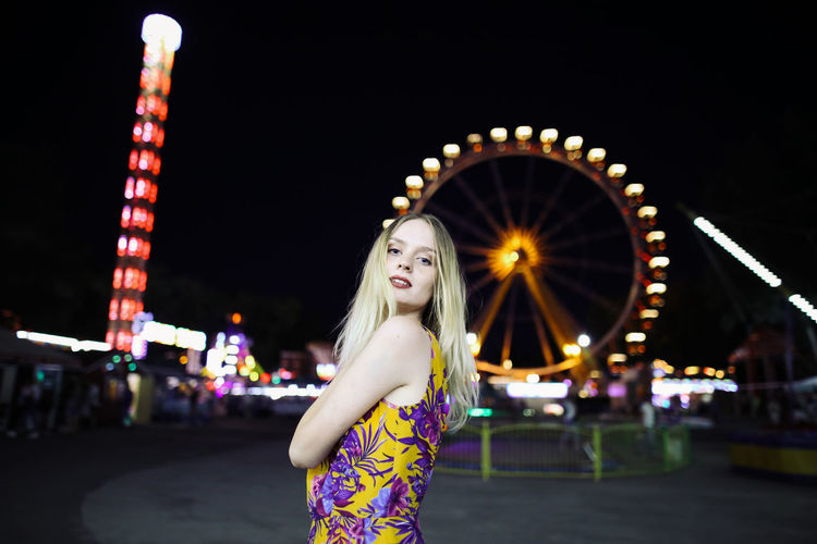 Girl at night in an amusement park against the backdrop of a ferris wheel. 