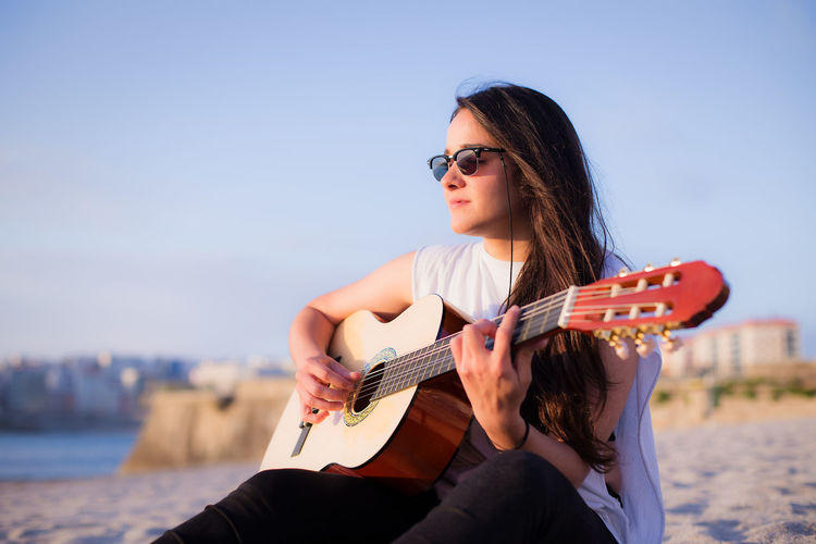 Young woman playing guitar against sky
