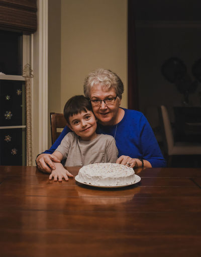 Young boy sitting with grandmother at table with a cake.