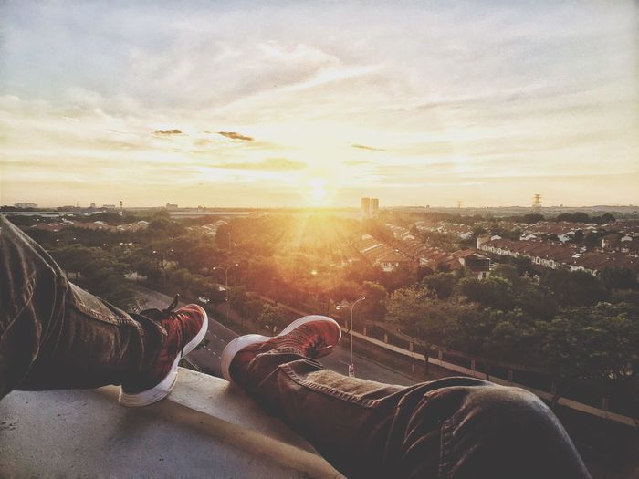 Low section of man sitting on terrace against sky during sunset