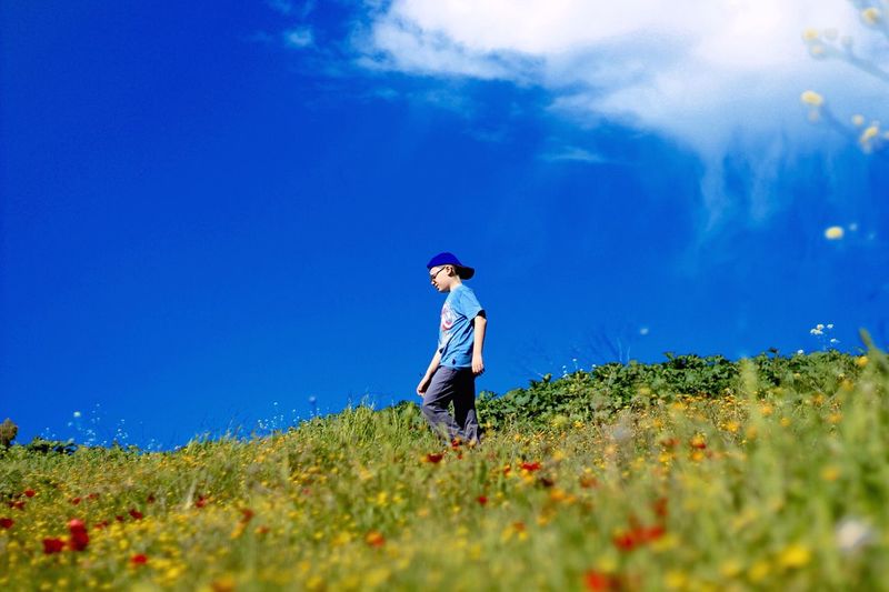 Low angle view of boy walking on grassy hill against sky during sunny day