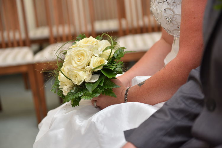 Midsection of bride with roses bouquet sitting on chair during wedding ceremony