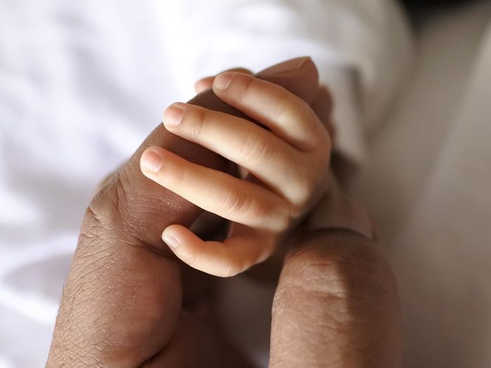 Cropped image of father holding newborn hand on bed