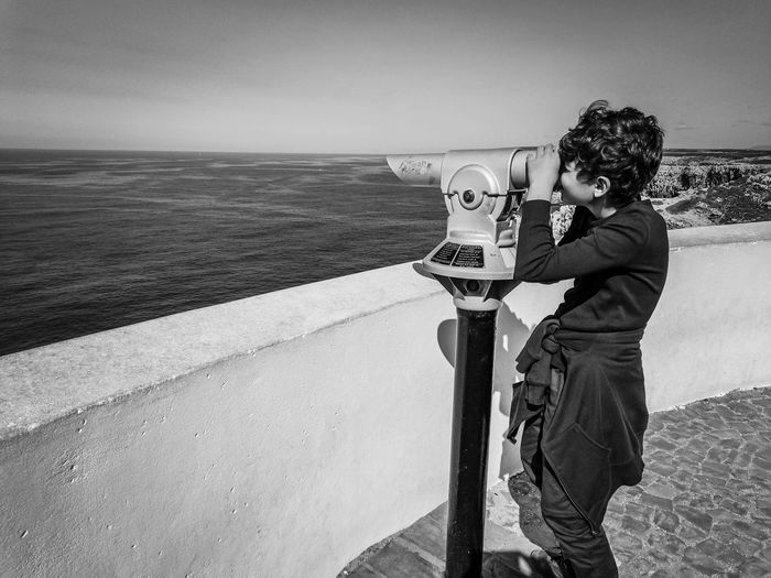 Boy looking at the sea through binoculars, in sagres, portugal.