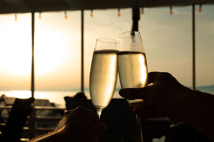 Hands holding glasses of champagne with sky on background - celebration anniversary concept
