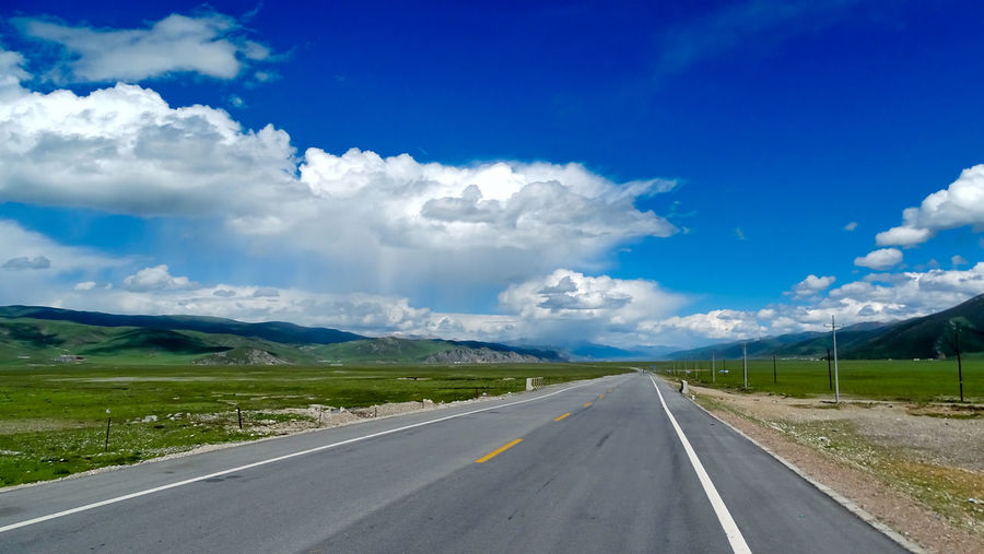 Empty road amidst landscape against blue sky