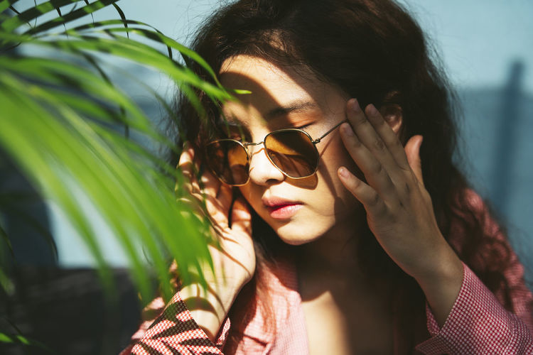 Close-up of woman wearing sunglasses sitting by plants