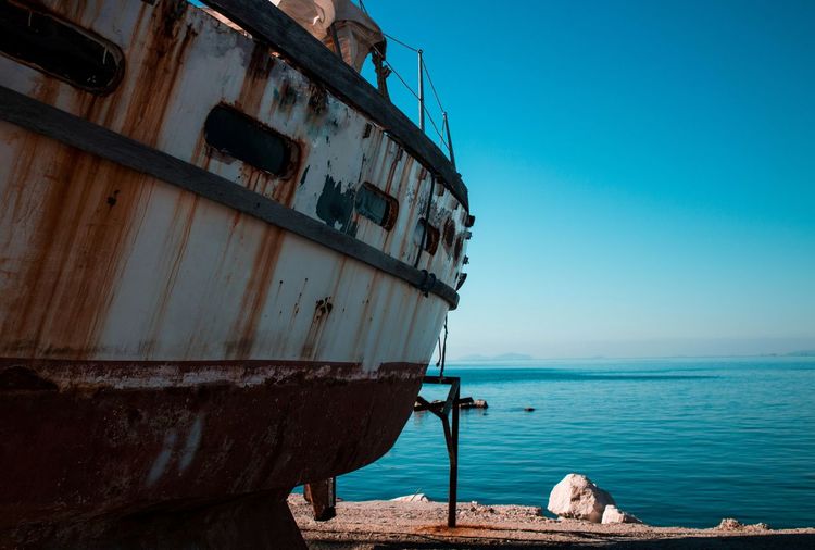 Abandoned boat moored at sea shore against sky