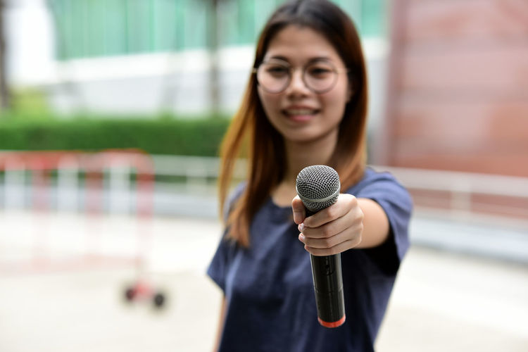 Portrait of female journalist with microphone standing against building