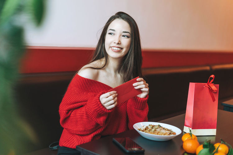 Beautiful asian woman in red clothes eating asian food with red envelope in cafe chinese new year