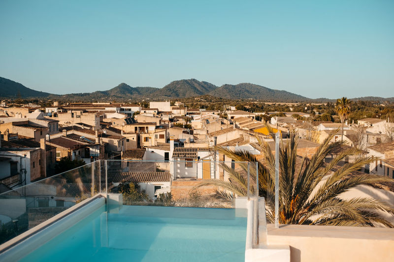 Picturesque scenery of town with typical residential houses surrounded by mountains from rooftop with pool on sunny day in mallorca