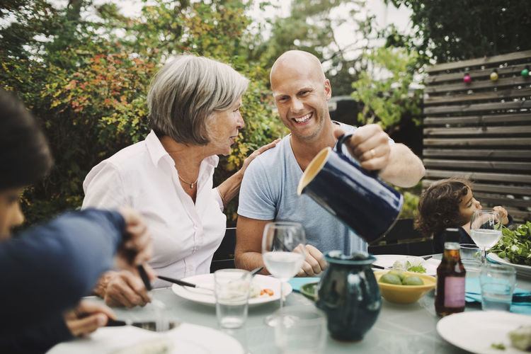 Happy man serving water to mother at outdoor dining table