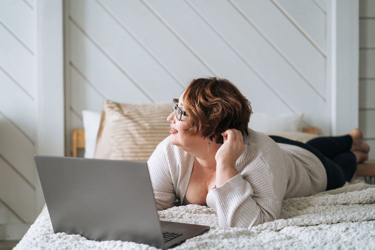 Young woman using laptop while sitting on bed at home