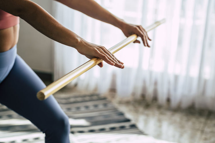 Midsection of woman holding stick while exercising at home