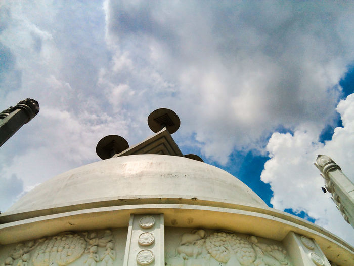 Low angle view of shanti stupa at dhauligiri against cloudy sky