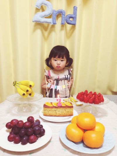 Cute girl standing in front of birthday cake on table at home