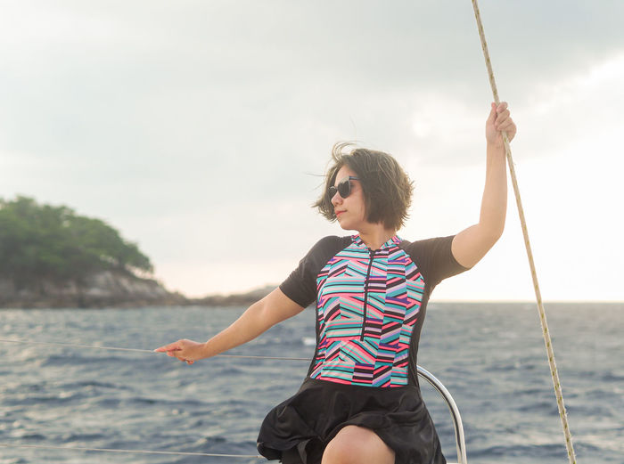 Side view of woman sitting on swing at yatch against sky