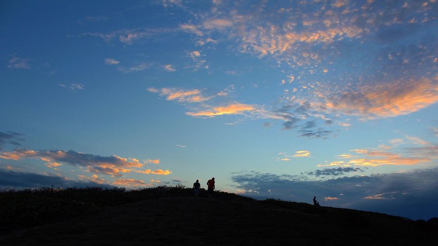 Low angle view of silhouette men on hill against sky during sunset