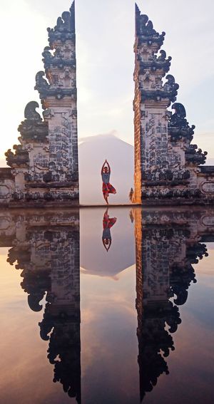 Reflection of man mediating by historic building in lake at sunset