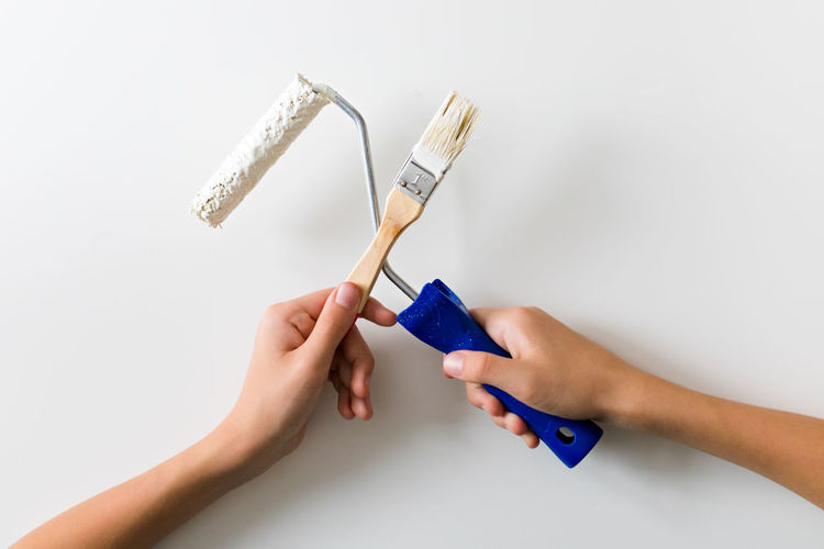 Cropped hand of woman holding paintbrush against white background