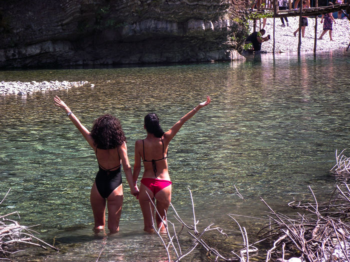 Rear view of female friends wearing bikini while standing in river