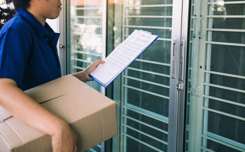 Midsection of delivery man holding paper and package while standing at entrance
