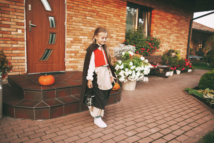Full length of girl standing by flowering plants against house