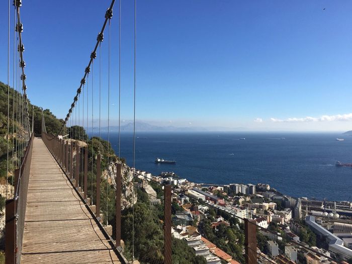 Suspension bridge over sea against clear blue sky