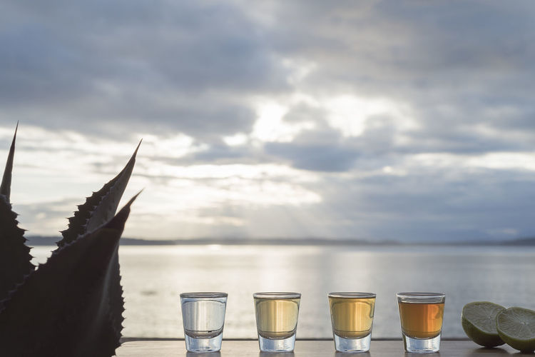 Tequila shots on table by sea against sky