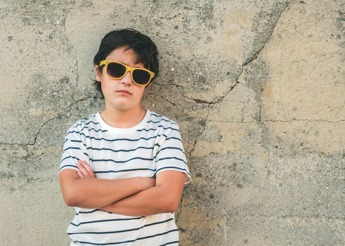 Boy wearing sunglasses standing against wall