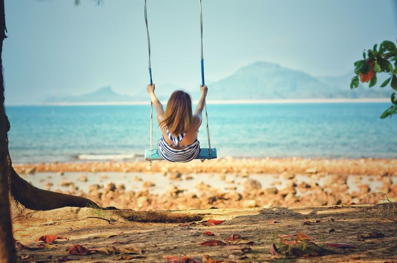 Rear view of woman swinging at on beach against sky