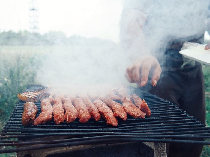 Midsection of man preparing barbeque meat in yard