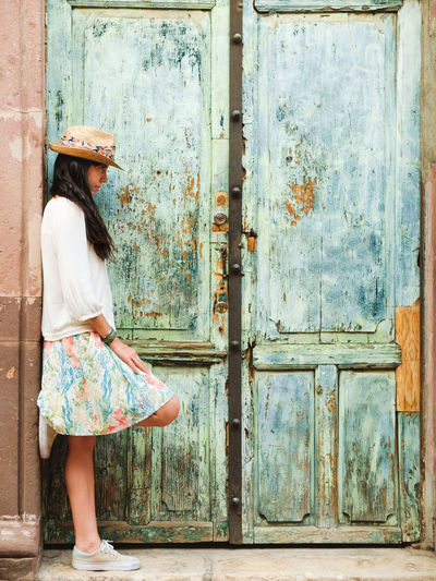 Side view of young woman posing by closed old door