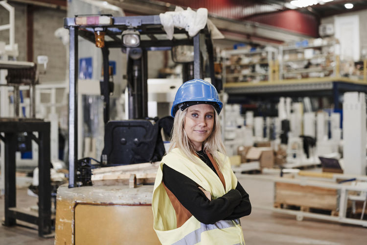Confident engineer standing with arms crossed in factory