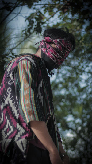 Side view portrait of man covering face standing against trees
