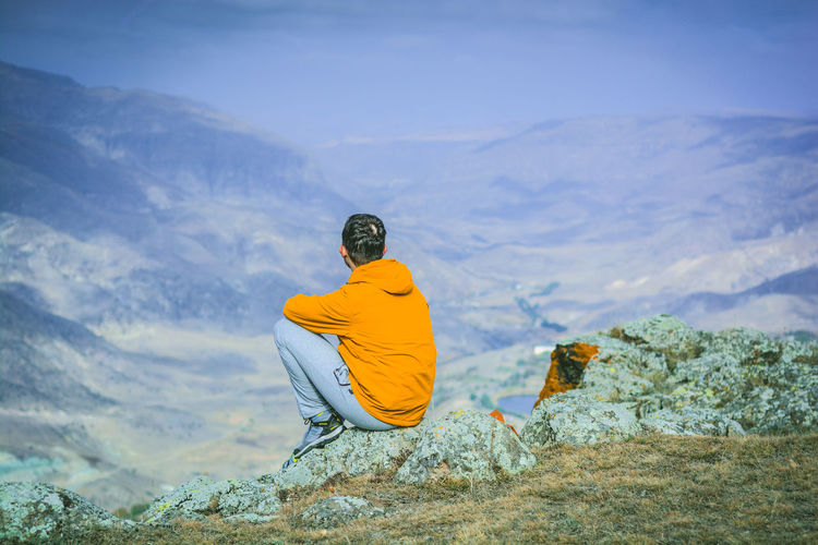 Man sitting on cliff against mountains