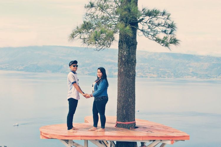 Full length of couple holding hands standing on heart shape by tree against sky