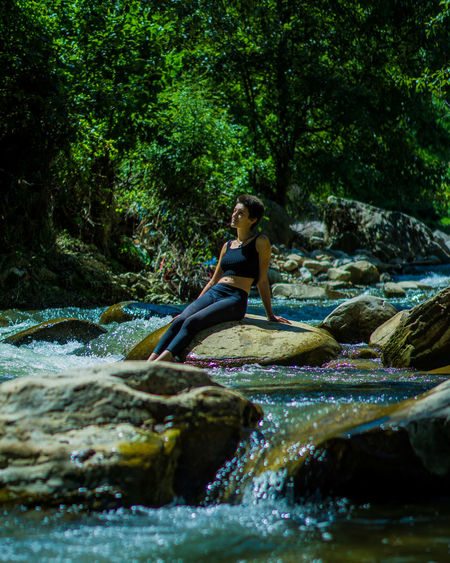 Side view of young woman sitting on rock in forest