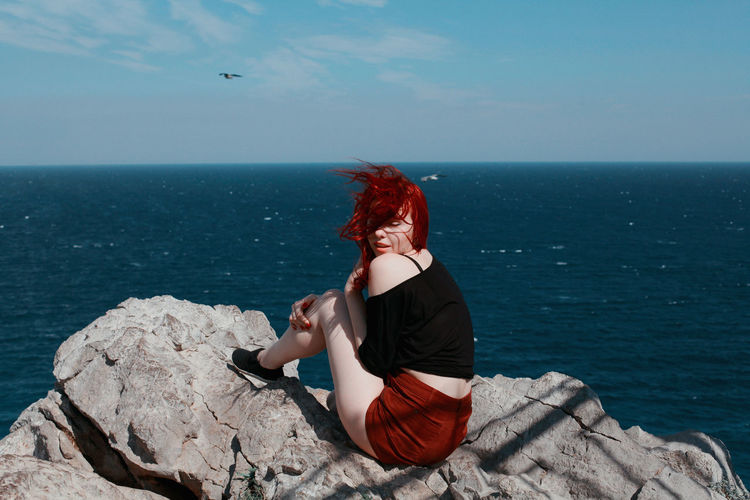 Woman sitting on rock by sea against sky