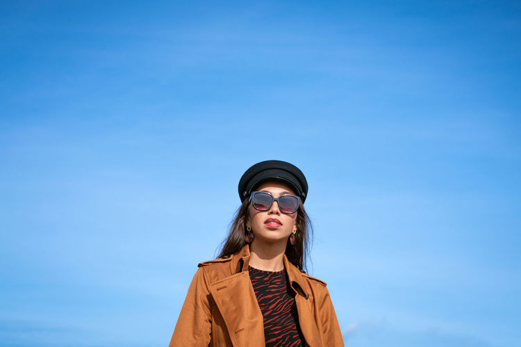 Portrait of young woman standing against blue sky
