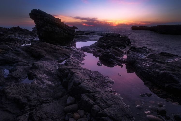 Rock formation at beach against sky during sunset
