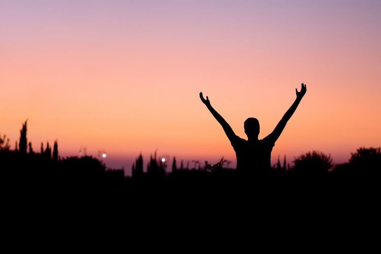 Silhouette man with arms raised standing against clear sky during sunset