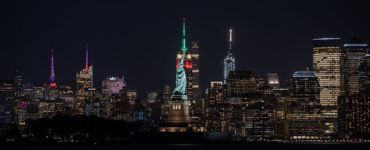 Illuminated buildings and statue of liberty in city at night
