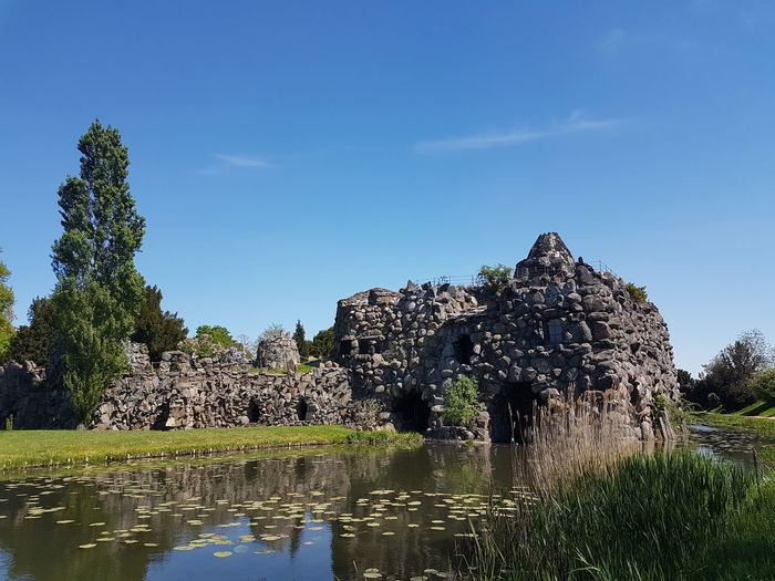Old ruin by pond against blue sky